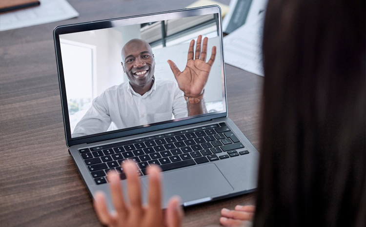 A person waves at another during a video call on a laptop, discussing important topics like mortgage fraud in Canada—one person visible on the screen and the other seen from behind, mortgage fraud canada