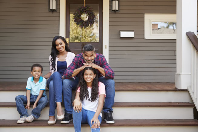 A family of four sits together on the front steps of their house, smiling at the camera, celebrating a new chapter made possible through mortgage-financing.